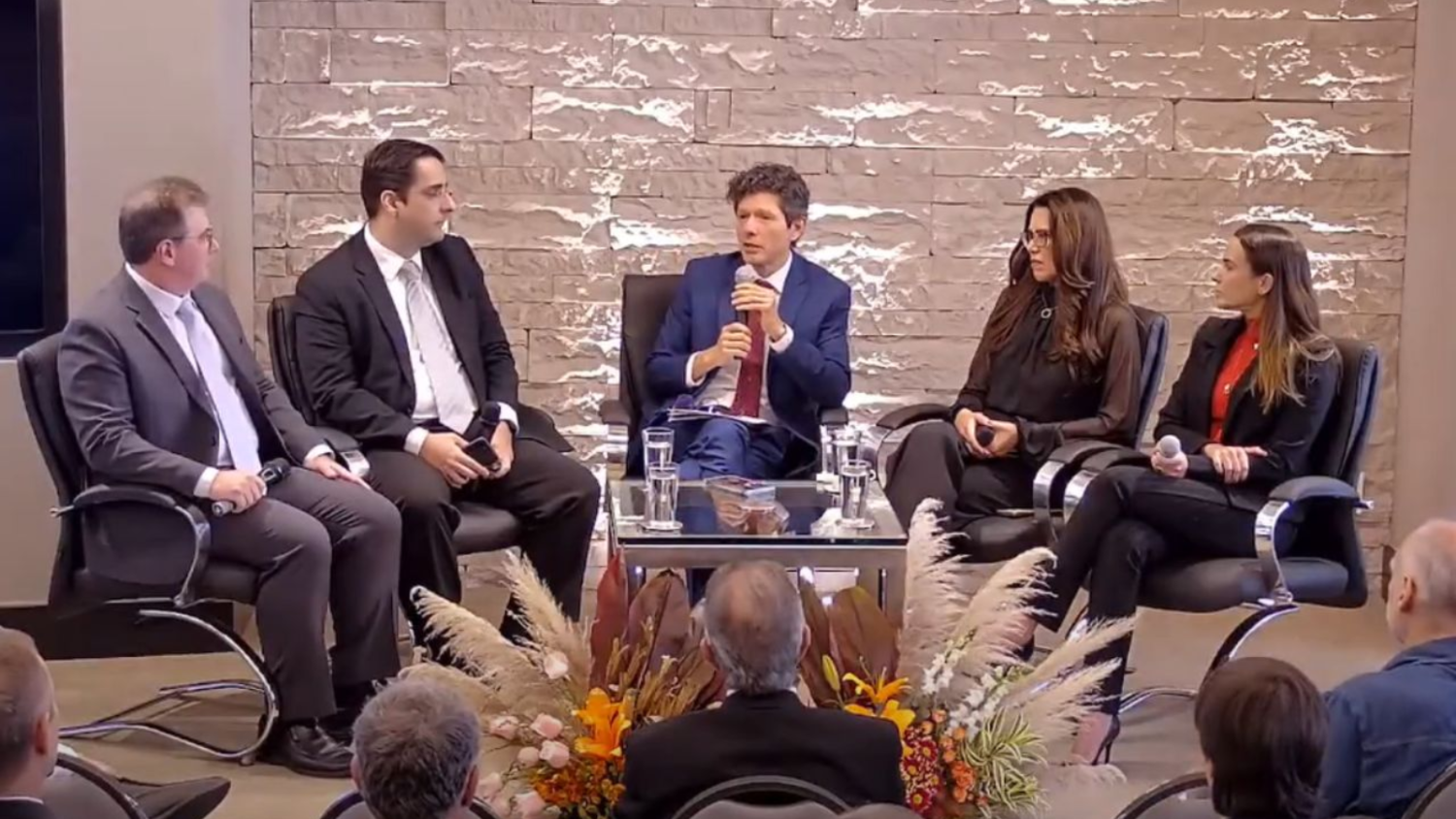 Participantes da roda de debates, sentados, em volta de uma pequena mesa de vidro