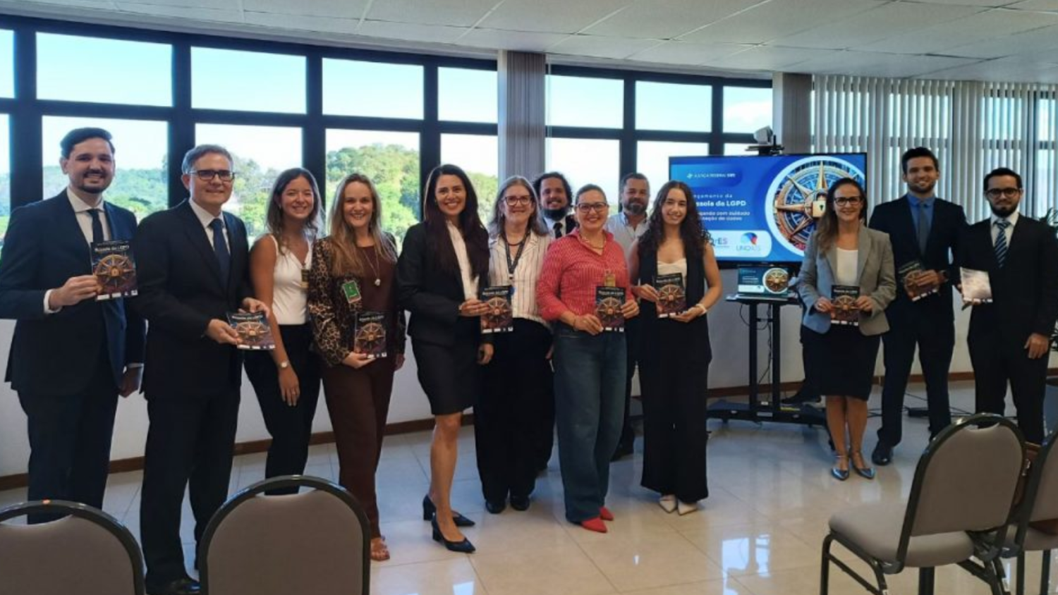 13 pessoas de pé, sendo 6 homens e 7 mulheres, todos com a cartilha nas mãos