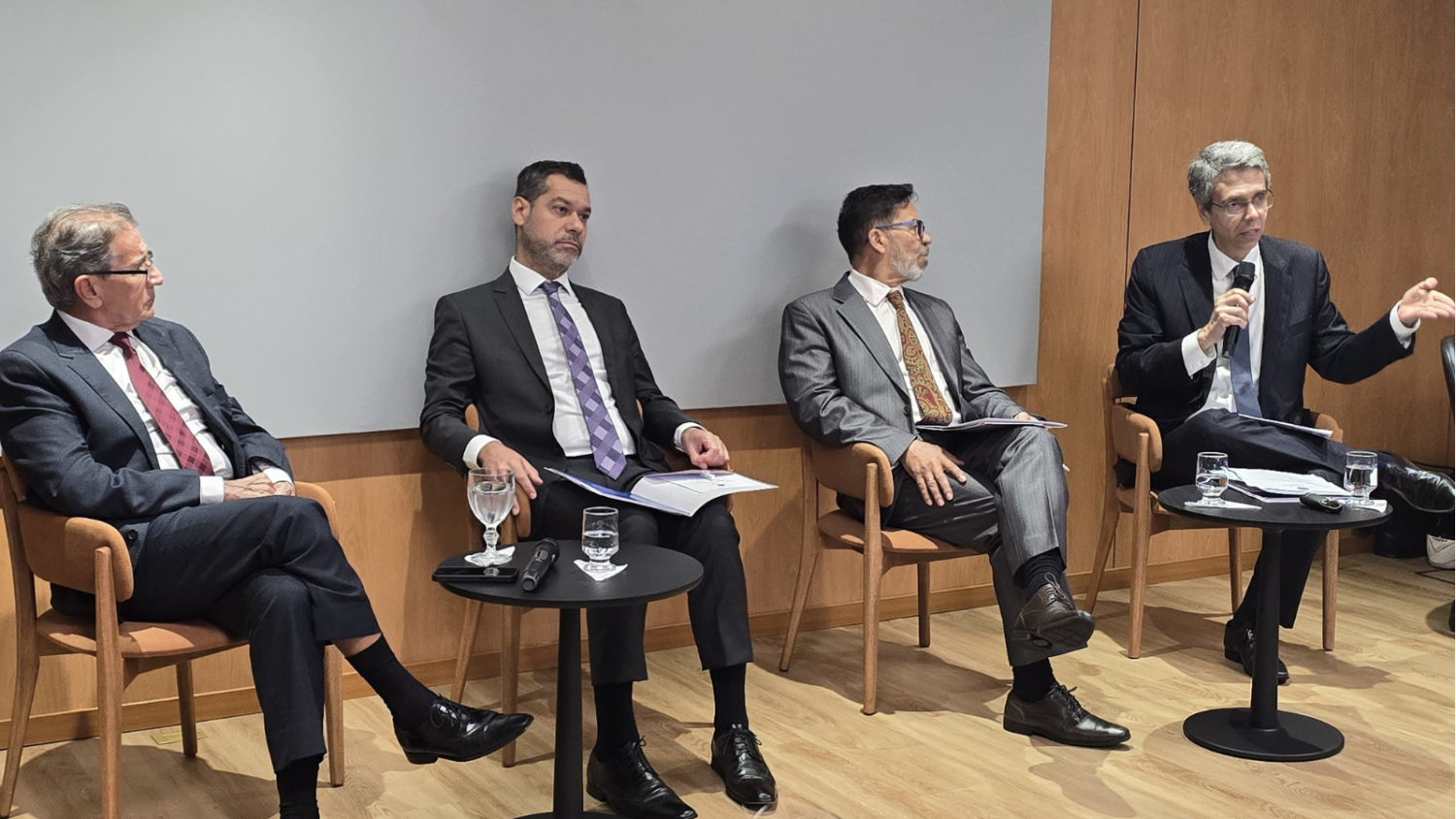 O desembargador federal Guilherme Camon fala ao microfone, sentado. Ao seu lado, três desembargadores