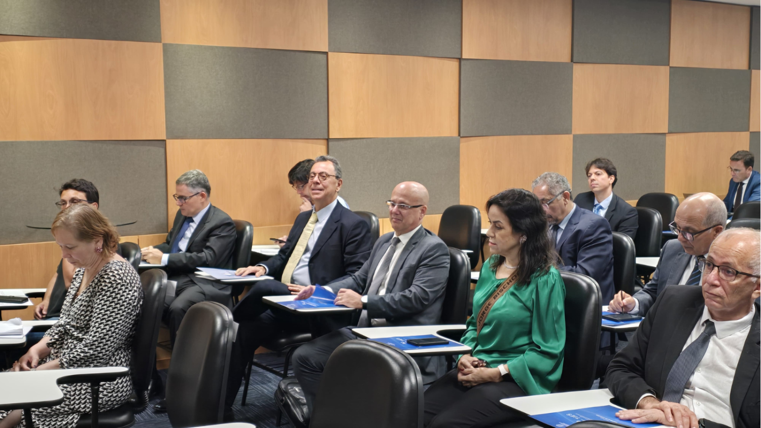 Magistrados e magistradas sentados no auditório, em cadeiras pretas. Dentre eles, o desembargador federal Aluísio Mendes