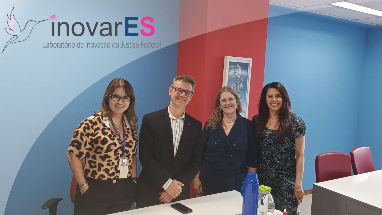 Três mulheres e um homem, numa sala com paredes nas cores azul e vermelho. Sobre a foto, a logomarca do InovarES
