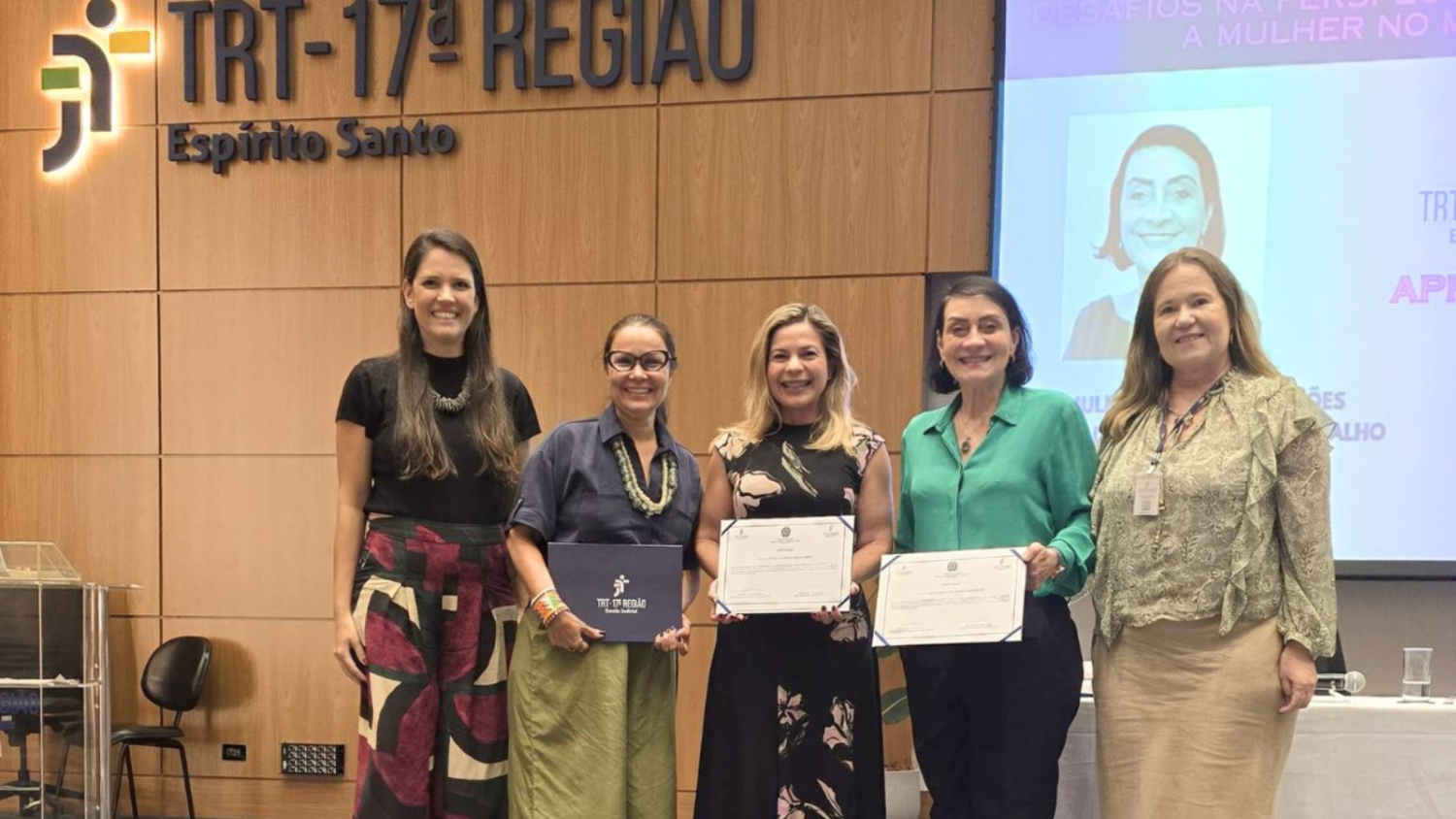 uma mulher e dois homens sentados ao redor de uma mesa redonda cinza claro, com computadores