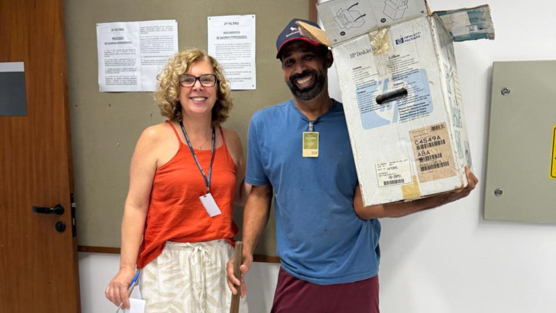 Uma mulher e um homem sorrindo para a câmera. Ele segura uma caixa média de papelão, com materiais dentro