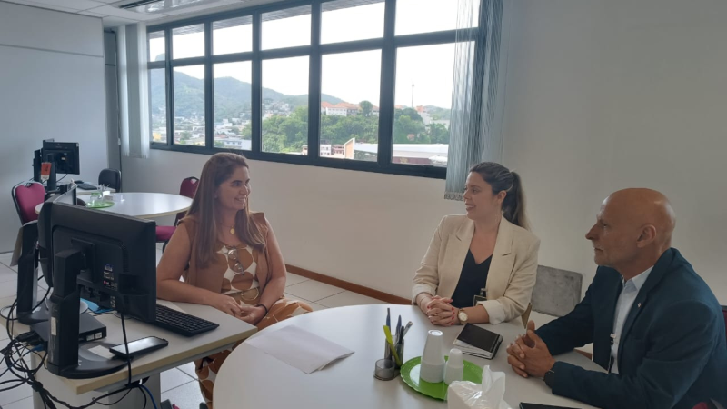 Duas mulheres e um homem conversam em volta de uma mesa redonda