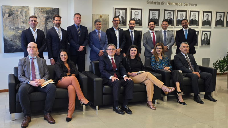 Grupo de magistrados e autoridades posando para foto em ambiente interno. Parte está sentada em sofás e parte em pé atrás, diante de uma parede com quadros de ex-diretores do foro. Todos vestem trajes formais.