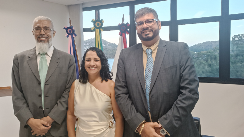 Pessoas posam para uma foto em uma sala da Justiça Federal. Ao fundo, há bandeiras e uma janela com vista para uma área verde.