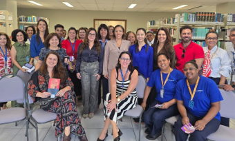 Grupo de cerca de 20 pessoas, em sua maioria mulheres, posando em pé e sentadas em uma biblioteca institucional, com estantes de livros ao fundo. Algumas seguram exemplares de livro. O ambiente é iluminado e formal, com clima de integração após atividade coletiva.