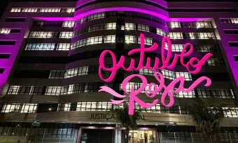 Fachada da sede da Justiça Federal, em Vitória, com iluminação na cor rosa. Sobre a foto, o texto "Outubro Rosa", em letras também cor-de-rosa