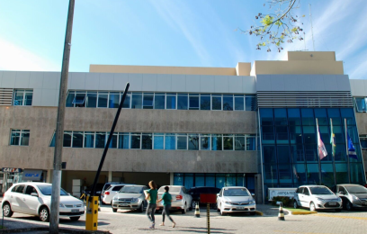 fachada de prédio horizontal com dois andares, carros estacionados em frente, e três bandeiras hasteadas