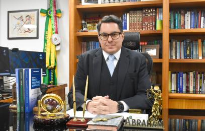 Desembargador federa Marcus Abraham sentado em seu gabinete. Usa terno preto com colete e gravata azul claro