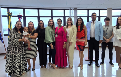 Oito mulheres e dois homens de pé, sorrindo para a foto. No colo de uma delas, uma bebê