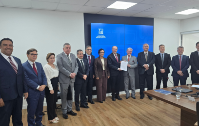 "Grupo de autoridades e representantes de tribunais posando para foto em ambiente interno, durante cerimônia de assinatura de cooperação técnica no Tribunal de Justiça do Espírito Santo. Ao centro, dois homens seguram o documento assinado."