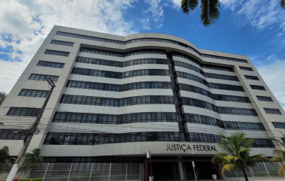 Fachada da sede da Justiça Federal, em Vitória: prédio de oito andares, mais horizontal que vertical, com formas curvas e janelas de vidro. 