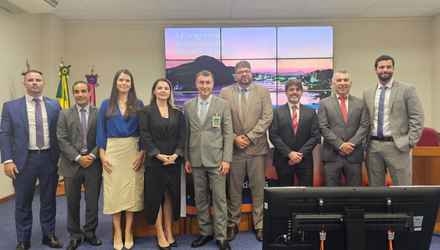Foto posada de sete homens e duas mulheres de pé, de frente para o auditório, sorrindo para a câmera