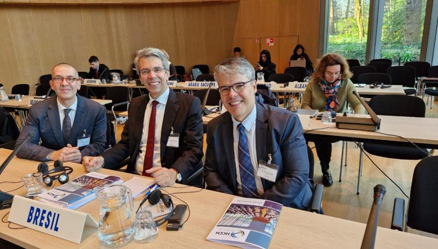 Três homens de terno sentados diante de balcão com prisma escrito "Brésil"