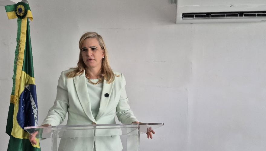 Mulher branca de cabelos loiros usando terninho com saia verde claro fala atrás de um púlpito transparente